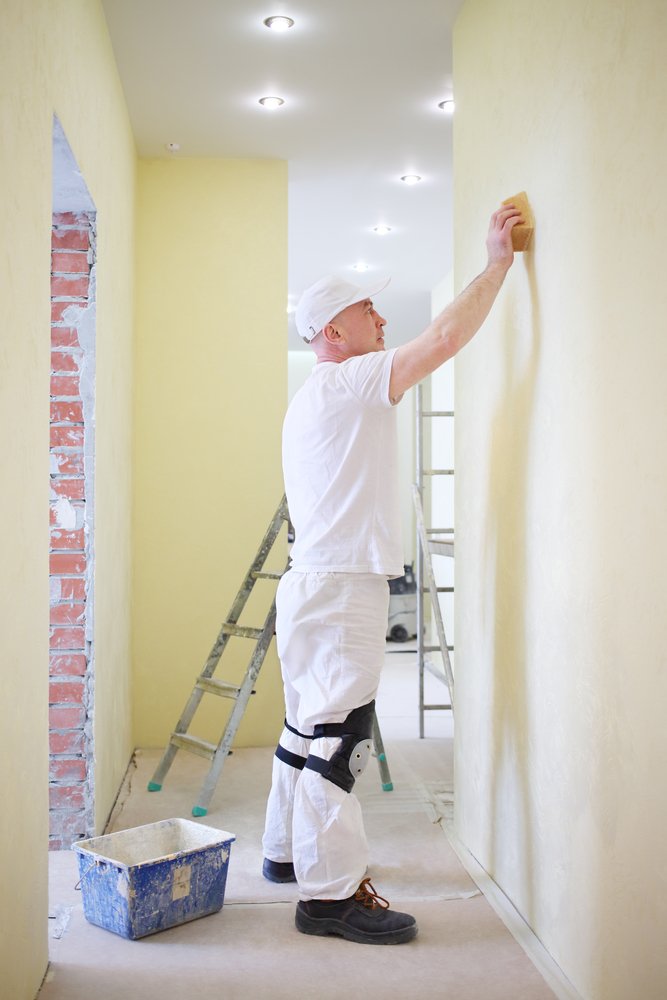 Een persoon die een muur repareert met vulmiddel, met gereedschap en reparatiemateriaal op de achtergrond.
