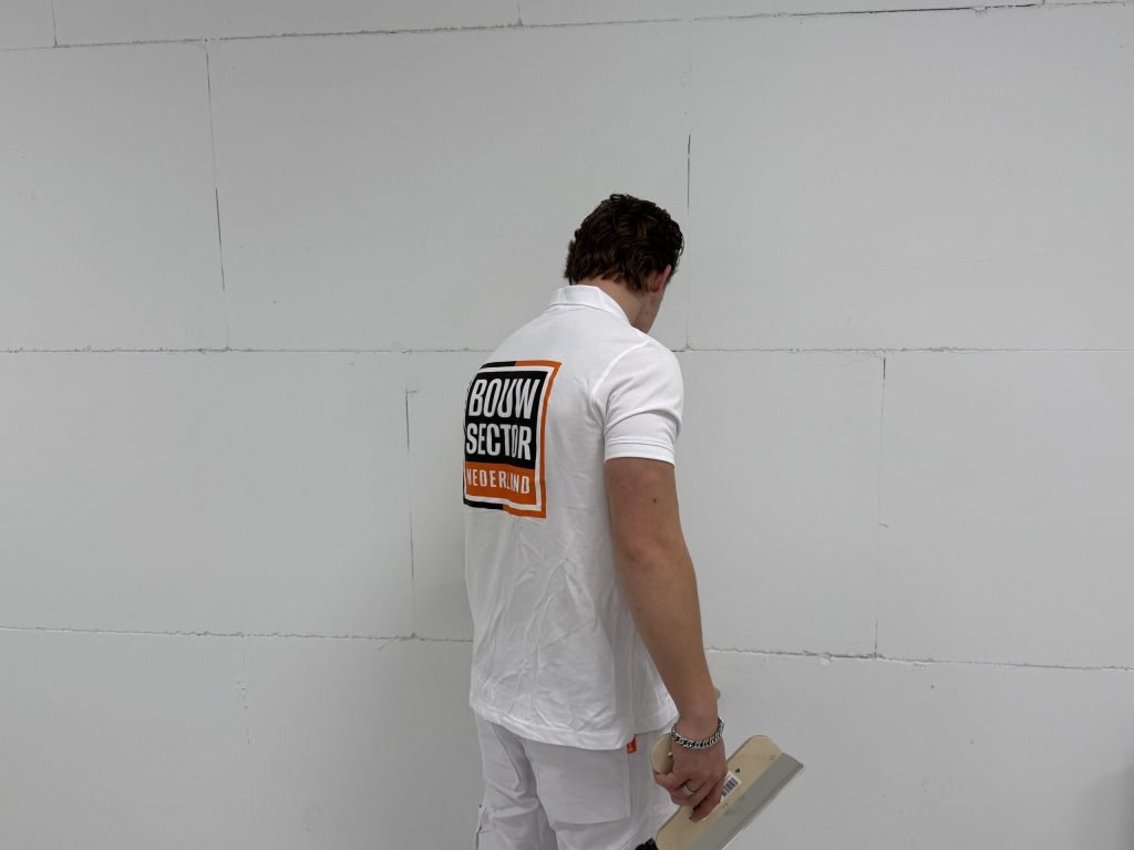 Stukadoor van Bouwsector Nederland bekijkt met een spaan in de hand een kale wand met voegen