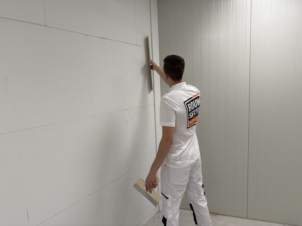 Stukadoor van Bouwsector Nederland trekt met een lange spaan het bovenste deel van een wand vlak