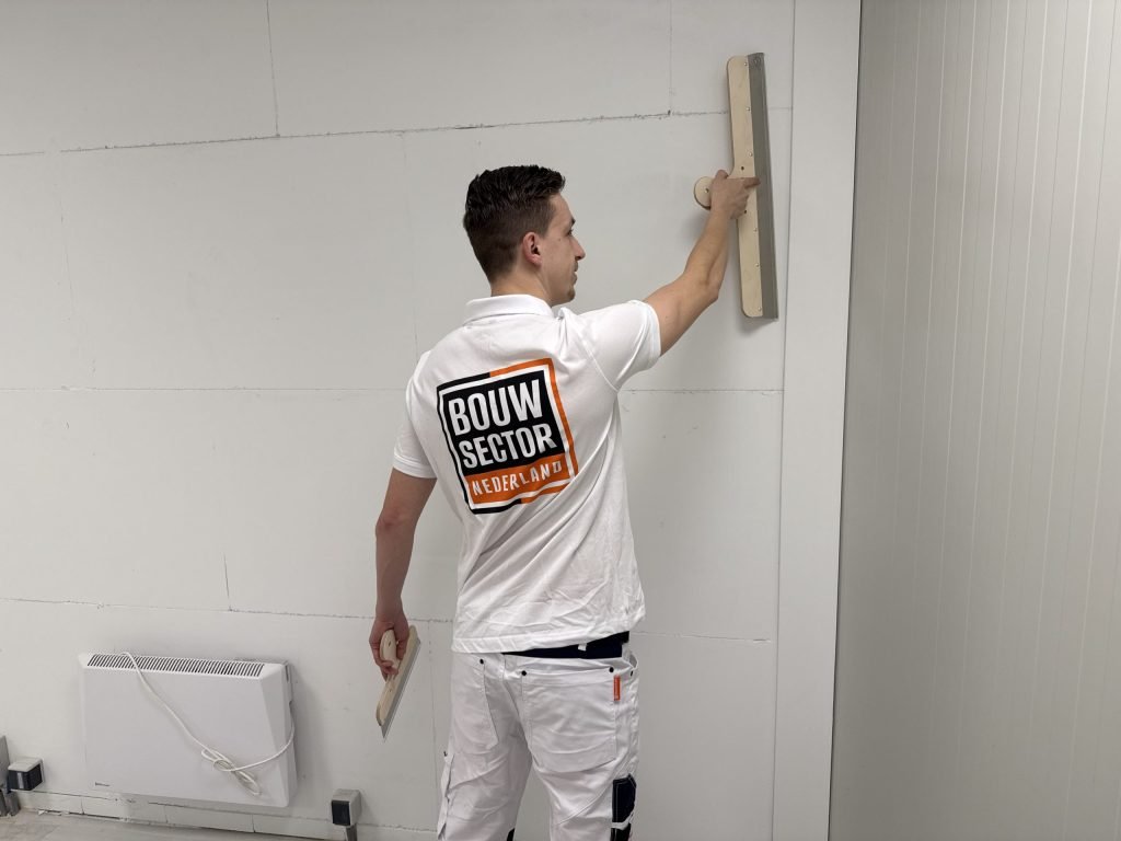Stukadoor van Bouwsector Nederland trekt met een brede spaan een wand vlak boven een verwarmingspaneel